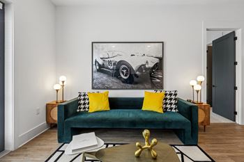 A living room with a green couch and a framed picture of a vintage car on the wall.